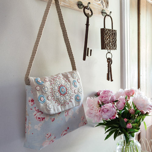 Styled shot of embroidered bag hanging up with pink flowers in vase