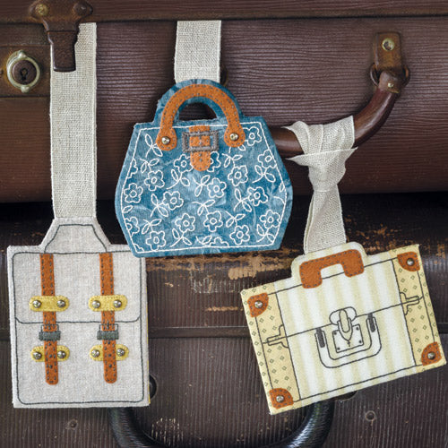 Styled shot of three different embroidered luggage-shaped luggage tags on vintage luggage