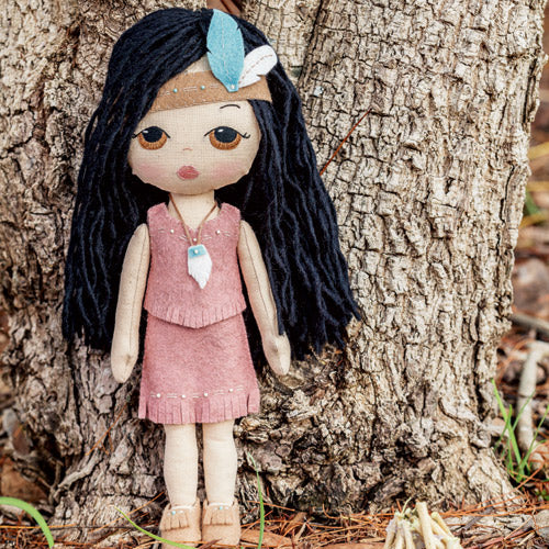 Styled shot of Pocahontas doll with accessories and embroidered detail against tree