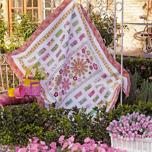 Styled shot of appliqué flower and patchwork quilt hanging up in garden