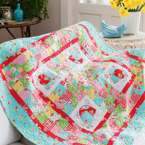 Styled shot of appliqué and embroidered bird patchwork quilt draped over couch