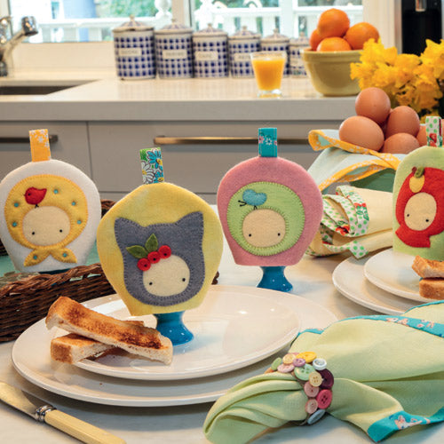 Styled shot of retro appliqué and embroidered retro-style egg cosies with egg cups, napkins and toast