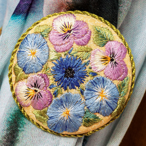 Styled shot of traditional-style embroidered flower brooch clipped onto scarf