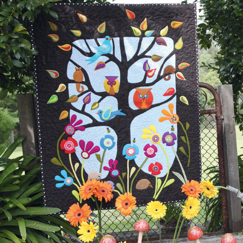Styled shot of appliqué owl, bird, flower and tree quilt hanging up in garden