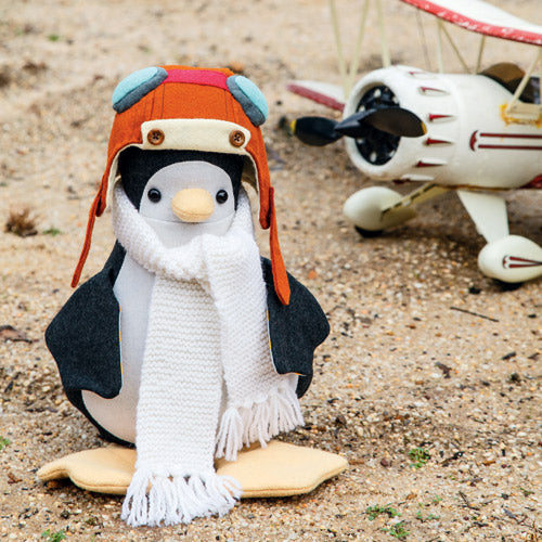 Styled shot of aviator penguin softie wearing knitted scarf and aviator helmet outdoors with toy plane