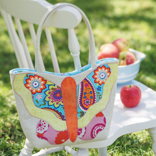 Styled shot of appliqué butterfly handbag on chair with apples