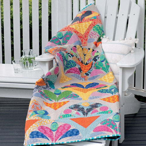 Bright, modern clam quilt with appliqué embellishment draped over outdoor chair