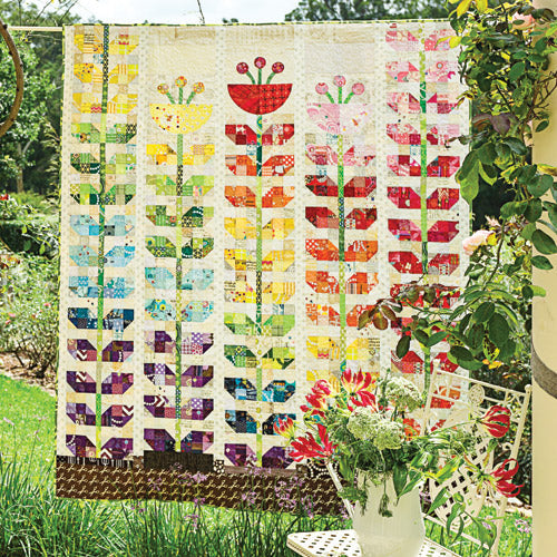Styled shot of patchwork and appliqué sprouting flowers quilt hanging up in garden