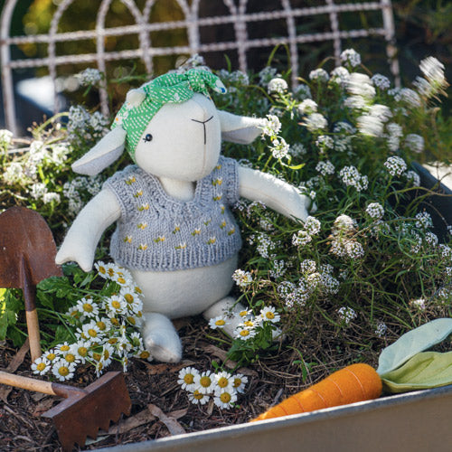 Styled shot of giddy goat soft toy with carrot toy, wearing knitted vest and headscarf in garden