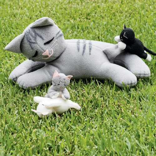 Styled shot of mother cat and three kitten soft toys playing on grass