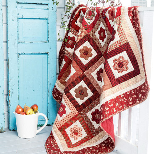 Styled shot of english paper pieced hexagon flower quilt draped over railing