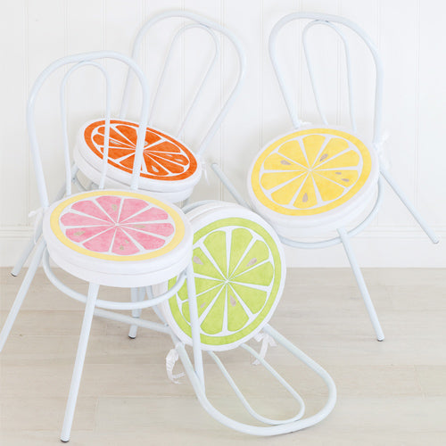 Styled shot of orange, lemon, lime and grapefruit appliqué chair cushions on white chairs