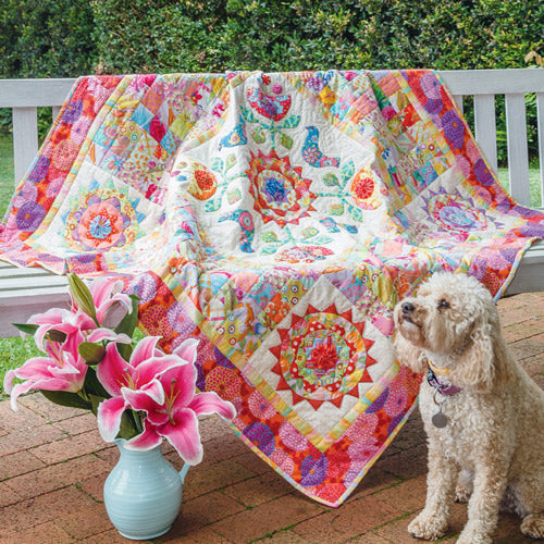 Styled shot of bird and flower appliqué and patchwork bright modern quilt with dog and flowers