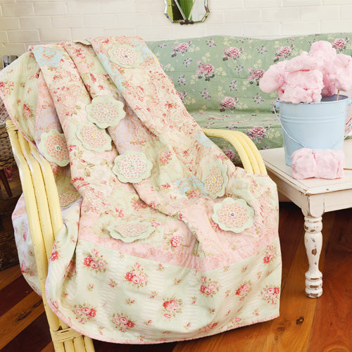 Styled shot of appliqué flower and patchwork pretty quilt draped over chair